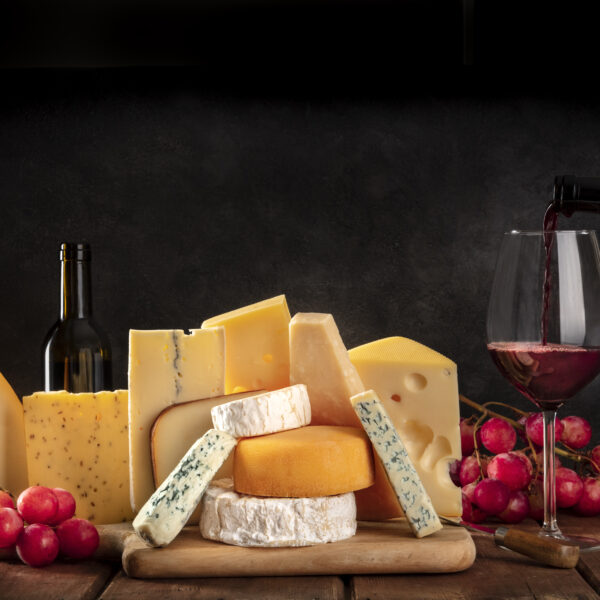 Cheeses with grapes and pouring wine, a side view on a dark background with copy space